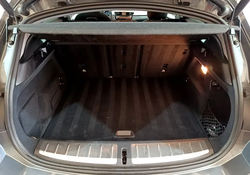 Coffre ouvert noir du BMW X2 xDrive25e vu de l'arrière, avec éclairage intérieur et filet de rangement latéral.