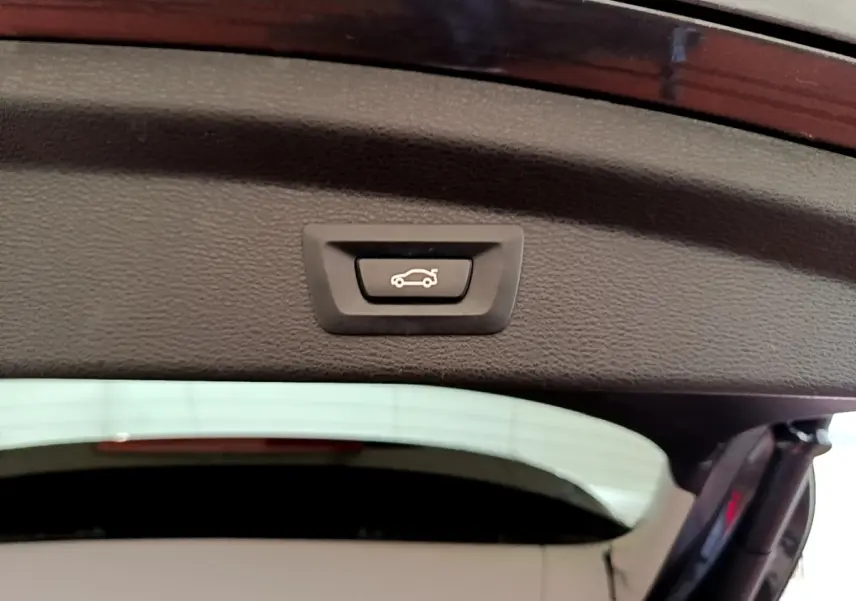 Bouton d'ouverture électrique du coffre sur la partie intérieure du hayon d'un BMW X2 hybride rechargeable, couleur sombre.