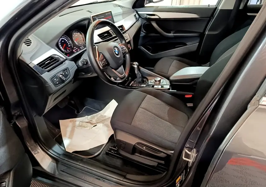 Vue intérieure côté conducteur de la BMW X2 xDrive25e noire, avec tableau de bord et volant multifonctions en cuir.