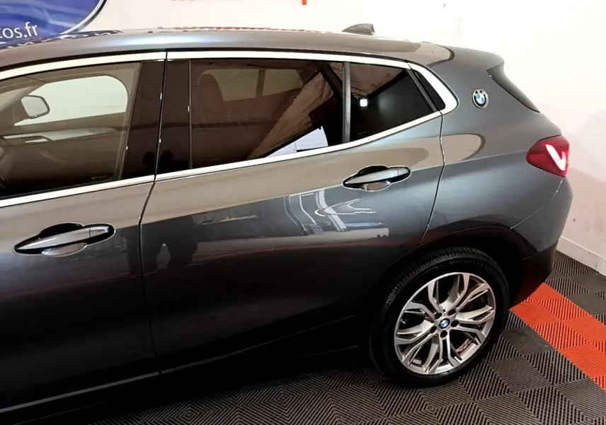 Vue latérale droite sur l'arrière d'un BMW X2 hybride rechargeable gris foncé avec jantes alliage et logo BMW sur l'aile arrière.