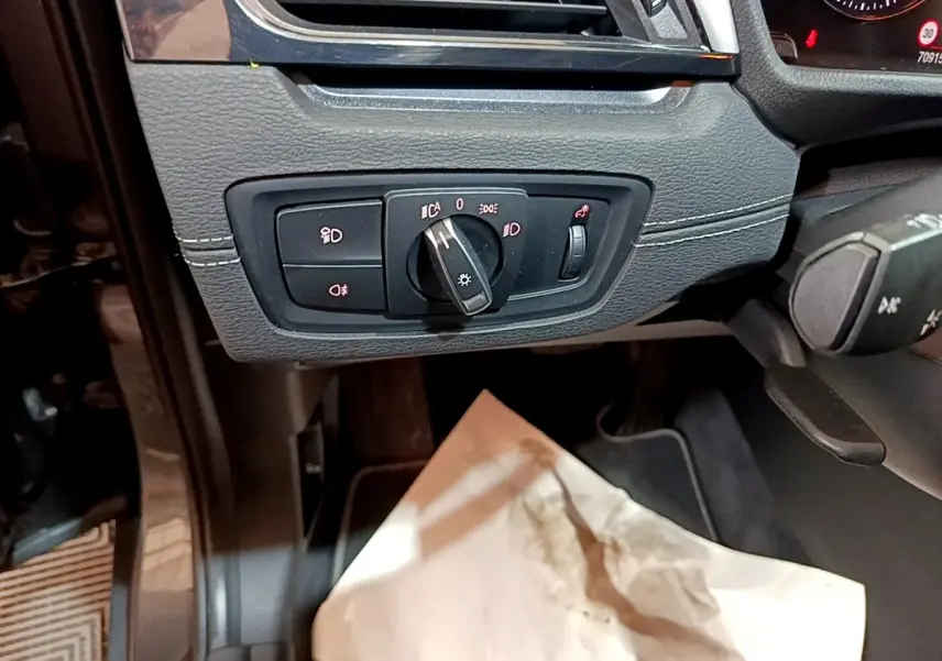 Gros plan sur le panneau de commande des phares à gauche du volant dans l'habitacle noir de la BMW X2 hybride.