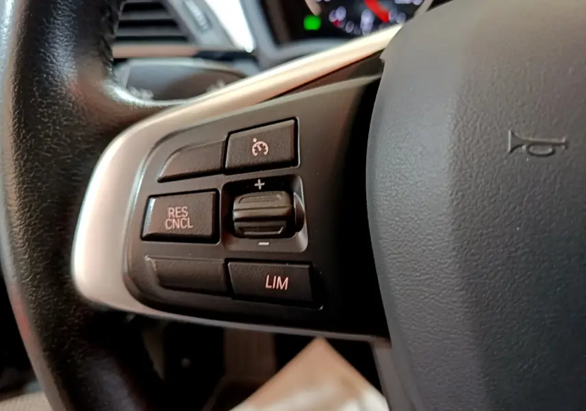 Gros plan sur les commandes noires du régulateur de vitesse au volant cuir noir de la BMW X2 hybride rechargeable.