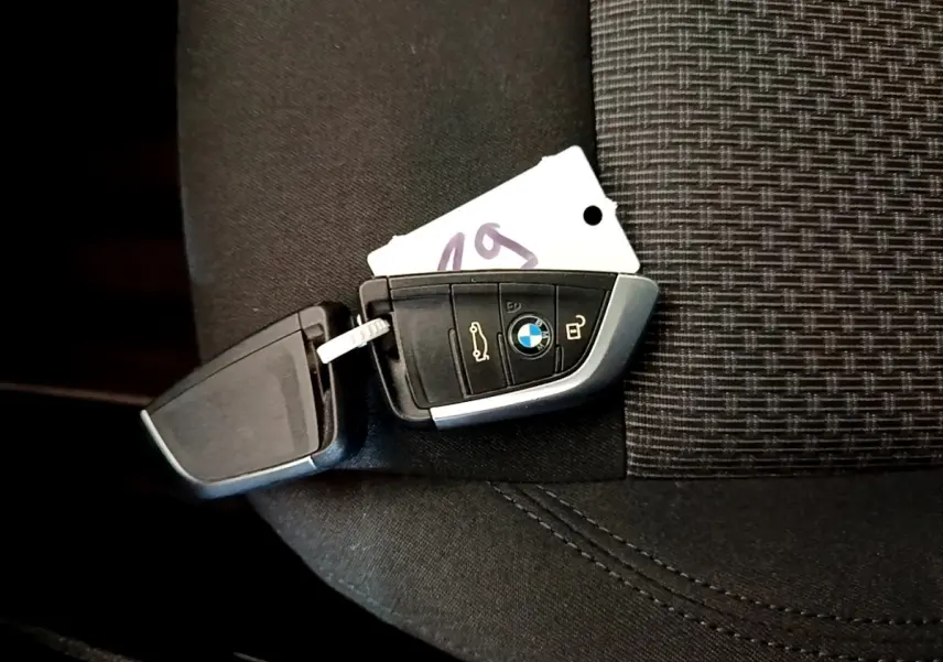 Clé BMW posée sur un siège tissu noir, montrant les boutons de verrouillage et ouverture du coffre.