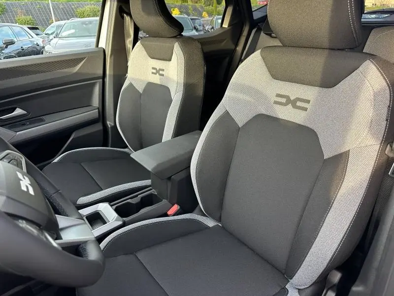 Vue intérieure du Dacia Duster 2025, sièges avant en tissu noir et gris avec logo DC brodé sur les appuie-têtes.