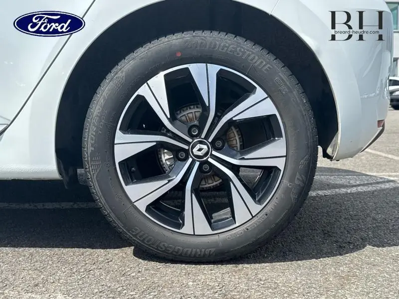 Gros plan sur la roue avant droite d'une Renault Clio blanche 2023 avec jante alliage bicolore et logo Renault central.