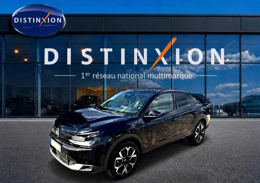Vue 3/4 avant droite de la Citroën C4 X noire 2025 avec jantes alu et phares LED devant un showroom Distinxion.