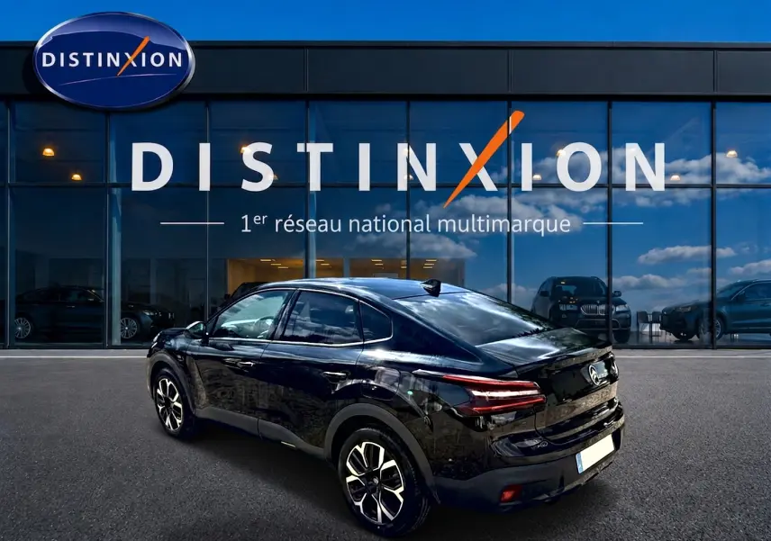 Vue 3/4 arrière droite d'une Citroën C4 X noire 2025 avec jantes alu et feux arrière LED, devant un showroom Distinxion.