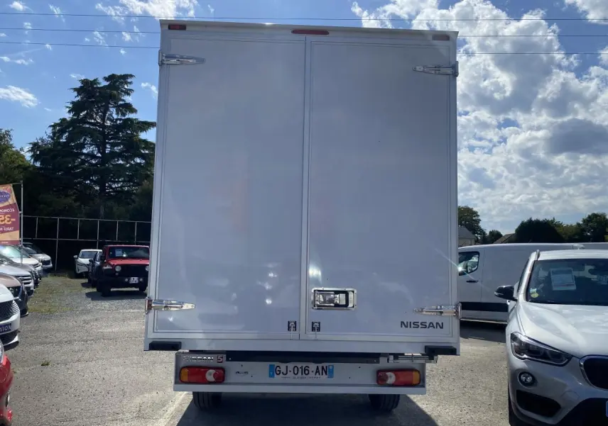 Vue arrière d'un utilitaire Nissan Interstar blanc avec caisse grand volume et portes fermées sous un ciel partiellement nuageux.