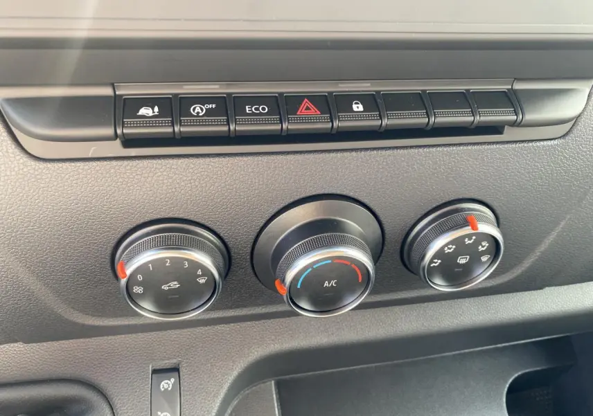 Gros plan sur les commandes de climatisation manuelle et boutons fonctionnels du tableau de bord du Nissan Interstar blanc.