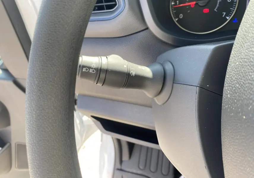 Gros plan sur la manette d'éclairage à gauche du volant dans un Nissan Interstar blanc, tableau de bord partiel visible.