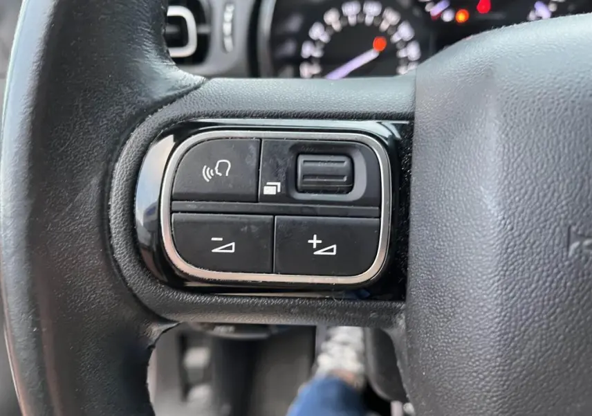 Gros plan sur les commandes audio au volant d'une Citroën C3 2019, finition Origins, volant en cuir noir.