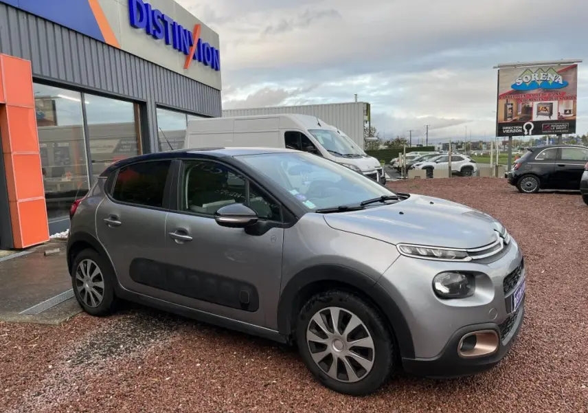 Citroën C3 gris foncé vue 3/4 avant droit avec protections latérales noires et coques de rétroviseurs noir brillant.