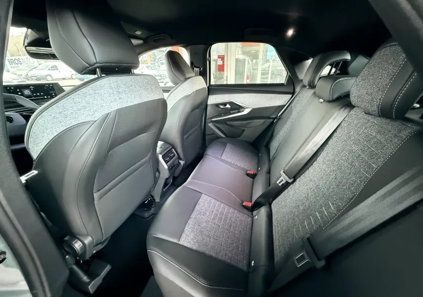 Vue intérieure arrière côté droit du Peugeot 3008 Hybrid 2025, sièges en tissu gris et cuir noir avec surpiqûres blanches.