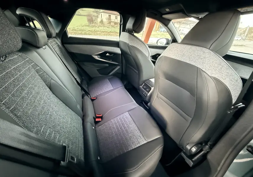 Vue intérieure arrière du Peugeot 3008 Hybrid 2025 montrant les sièges mixtes tissu et cuir avec surpiqûres contrastées.