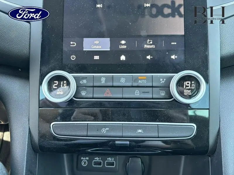 Gros plan sur la console centrale noire avec écran tactile et commandes de climatisation bi-zone d'une Renault Mégane gris Highland.
