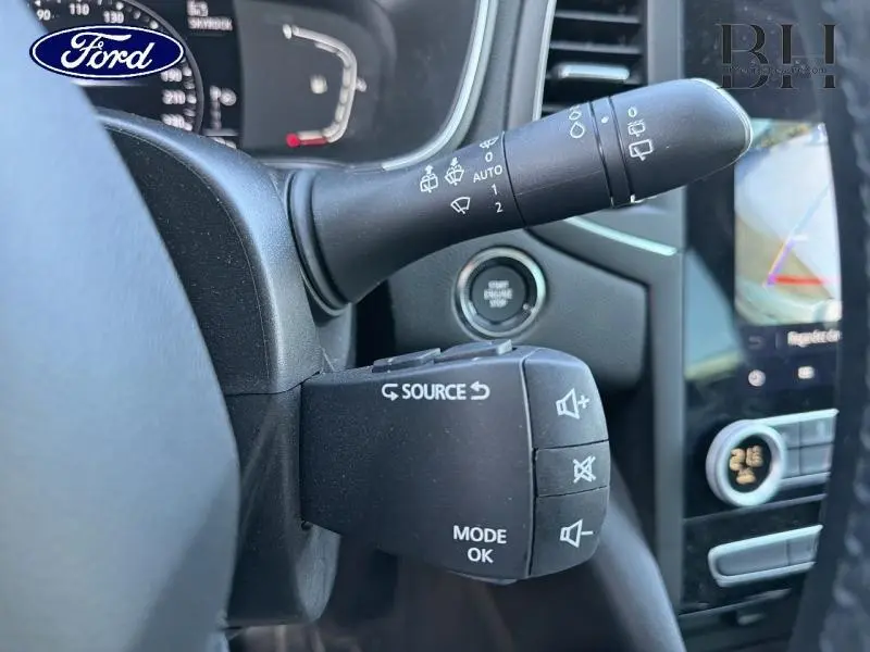 Gros plan sur la commande au volant et la manette d’essuie-glace d’une Renault Mégane gris Highland, avec écran tactile visible.