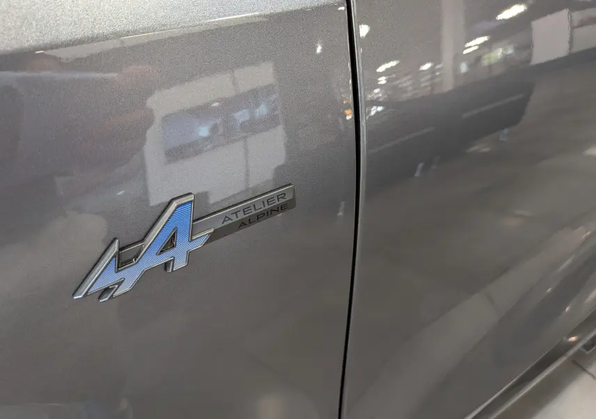 Gros plan sur l'emblème Atelier Alpine bleu sur la porte gris schiste d'une Renault Rafale 2026.