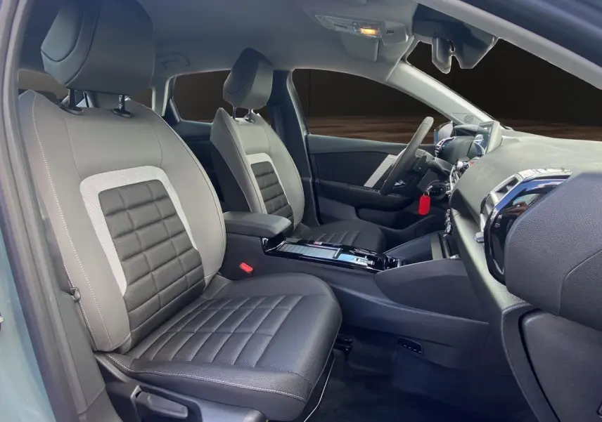 Intérieur avant de la Citroën C4 hybride 2025, sièges tissu gris noir avec console centrale et tableau de bord visibles.