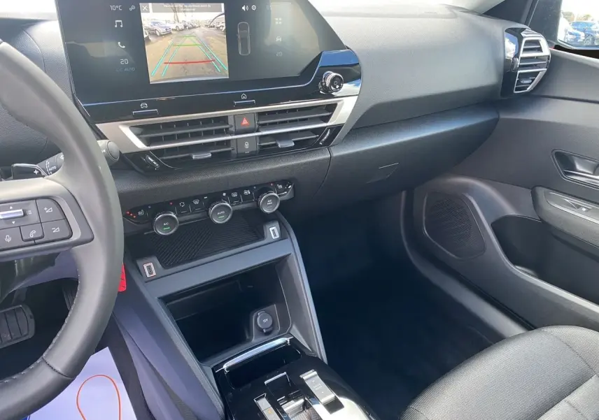 Intérieur avant droit de la Citroën C4 hybride 2025 avec tableau de bord noir et écran tactile 10 pouces en marche.