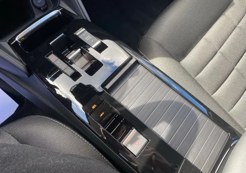 Gros plan sur la console centrale noire brillante et le siège tissu gris foncé de la Citroën C4 hybride 2025.