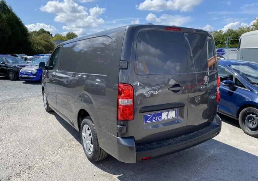 Vue 3/4 arrière droite d'un Peugeot Expert Fourgon gris platinium avec portes arrière tôlées et plaque Zero KM visible
