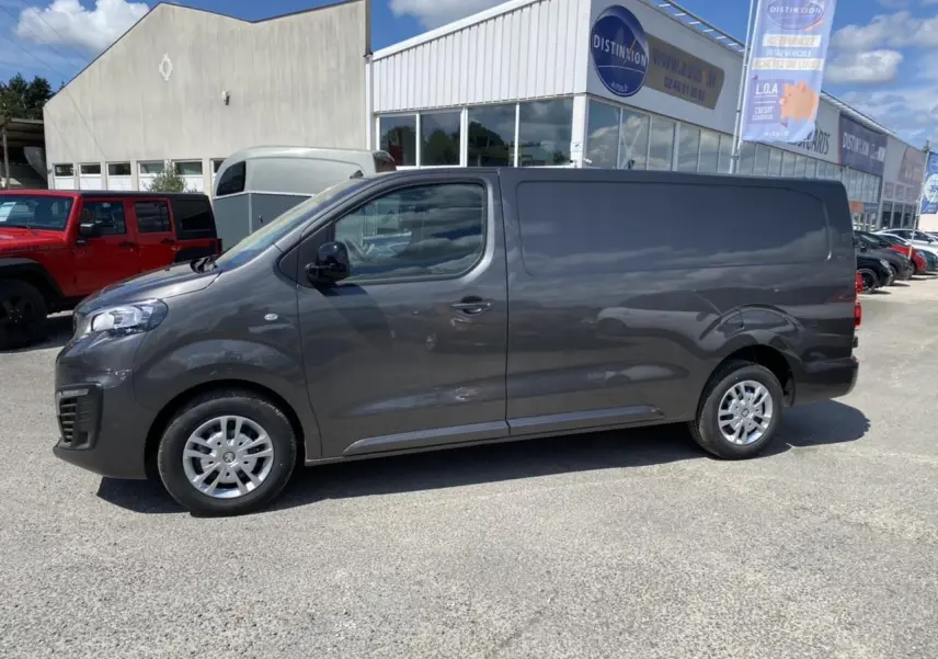 Vue latérale droite d'un Peugeot Expert Fourgon gris platinium stationné devant un bâtiment commercial.