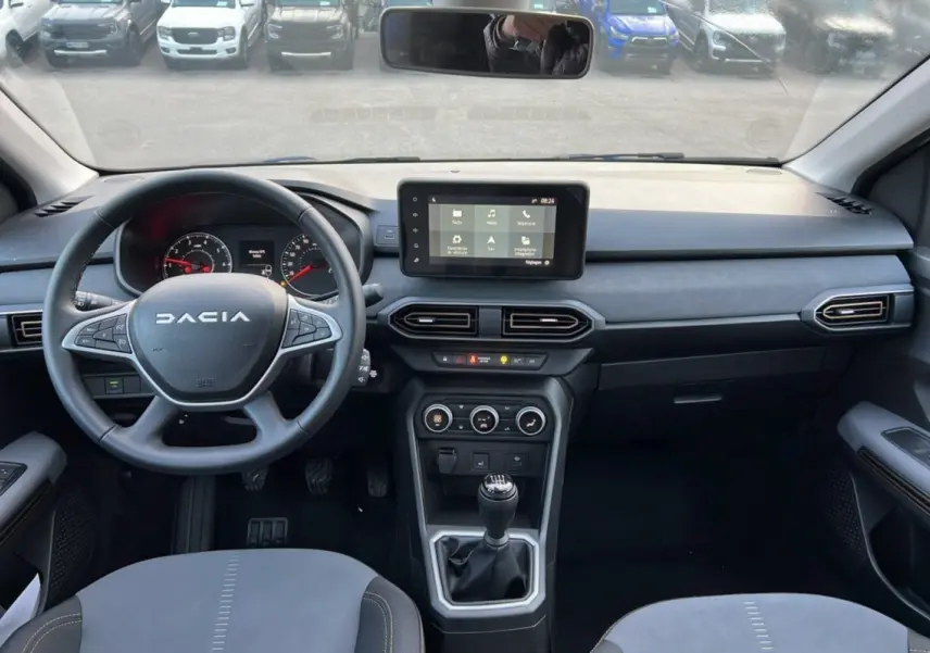 Vue intérieure avant du Dacia Sandero Stepway 2024, tableau de bord moderne avec écran tactile et levier de vitesses manuel.