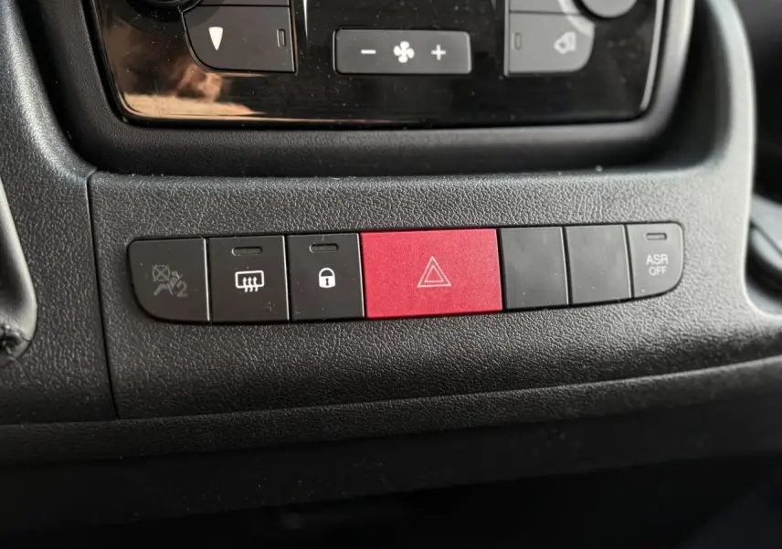 Gros plan sur la rangée de boutons du tableau de bord noir de l'Opel Movano Fourgon, avec bouton rouge de warning au centre.