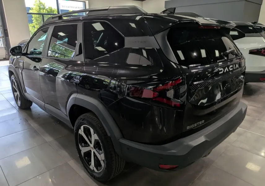 Vue 3/4 arrière droite du Dacia Bigster noir nacré avec jantes bicolores et toit noir en showroom.