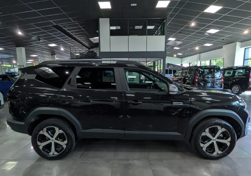 Vue de profil côté gauche d'un Dacia Bigster noir nacré 2026 en showroom, avec jantes bi-ton distinctives.