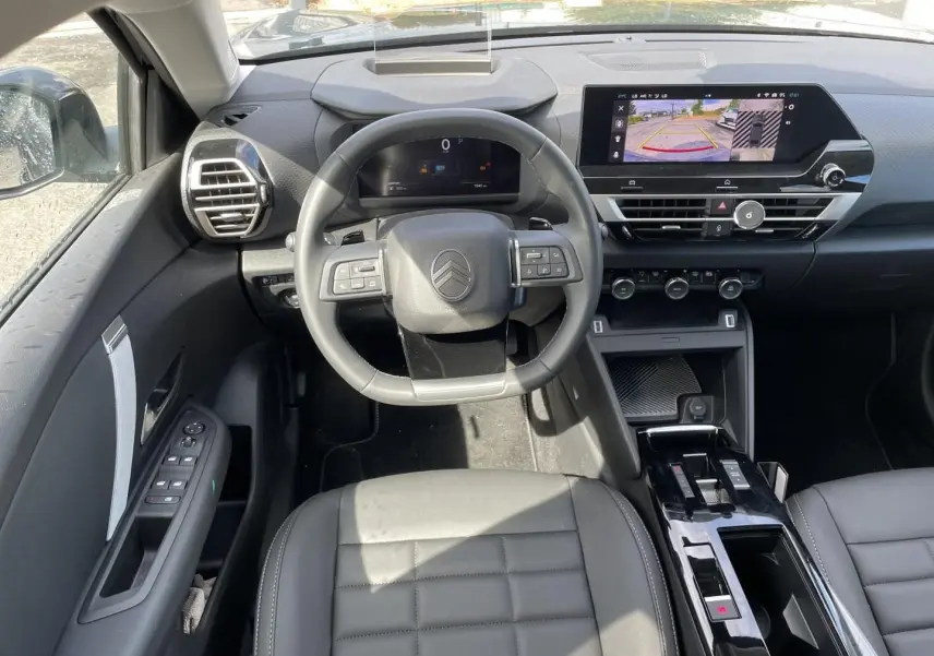 Vue intérieure avant centrée sur le volant cuir et tableau de bord avec écran tactile affichant la caméra de recul du Citroën C4 X noir.