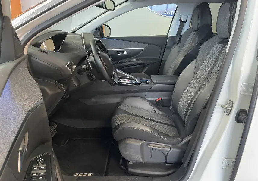Vue intérieure côté conducteur du Peugeot 5008 blanc nacré 2019, sièges tissu et cuir, tableau de bord moderne avec écran central.