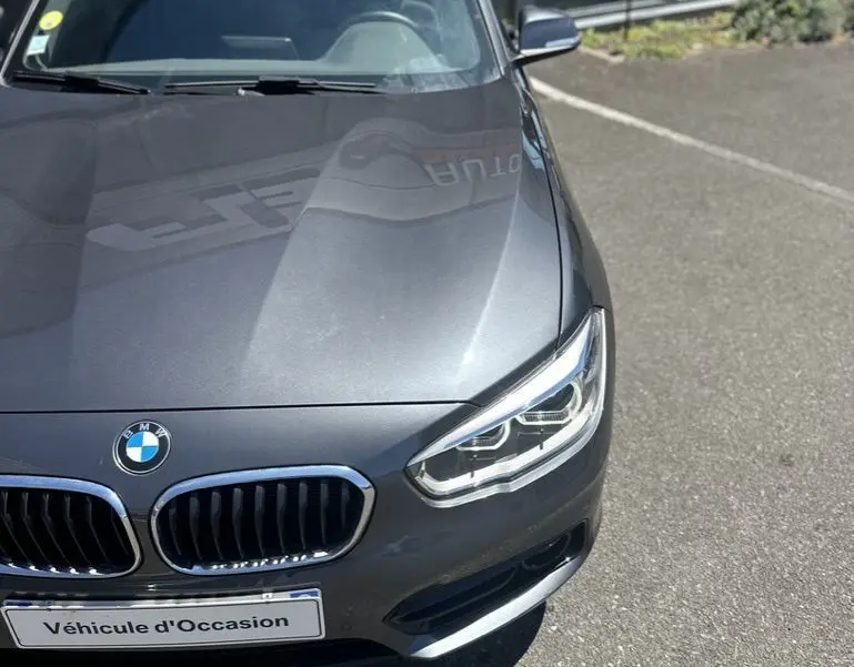 Vue 3/4 avant droite d'une BMW Série 1 F20 gris foncé avec calandre double haricot et phares LED visibles.