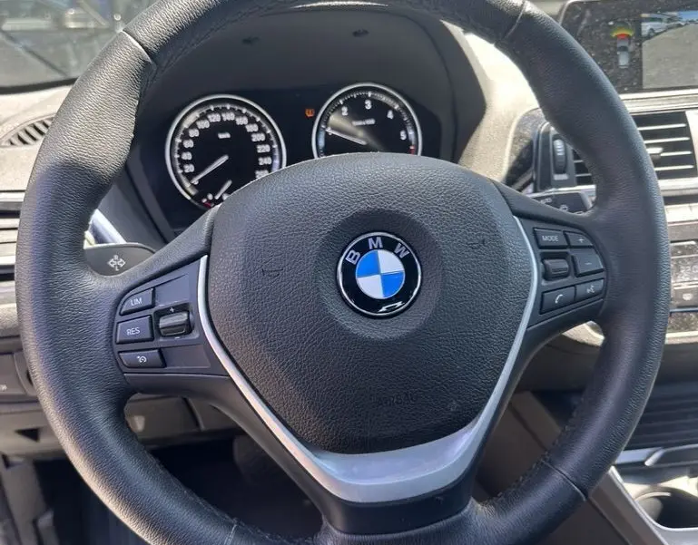 Vue rapprochée du volant noir de la BMW Série 1 F20 116D 2019 avec commandes intégrées et tableau de bord visible.
