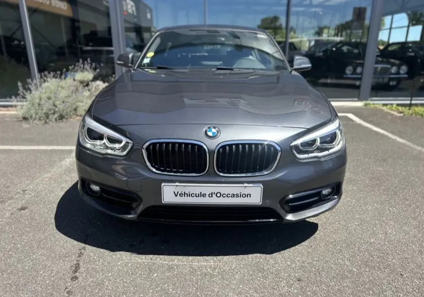 Vue frontale d'une BMW Série 1 F20 gris foncé de 2019 avec calandre double haricot et phares LED, en vente d'occasion.