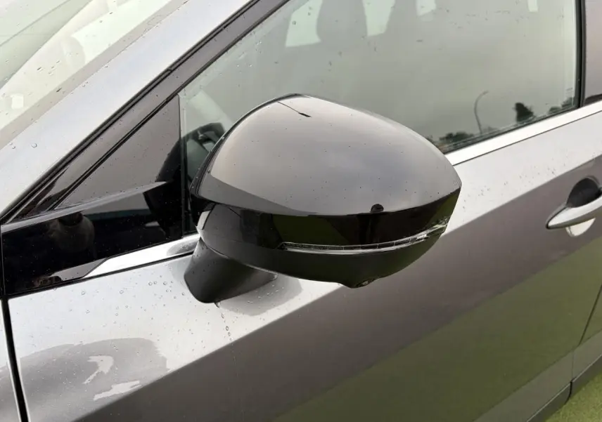 Gros plan sur le rétroviseur droit noir brillant du Nissan Qashqai III gris métallisé avec gouttes d'eau visibles.