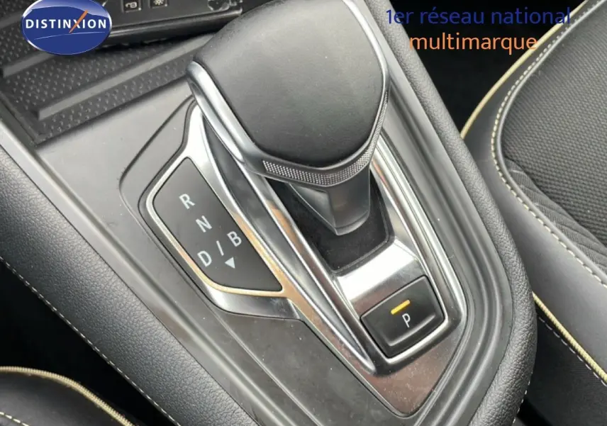 Le levier de vitesse automatique noir et chrome de la Renault Symbioz 1.6 E-TECH, entouré de sièges tissu noir avec surpiqûres beige.