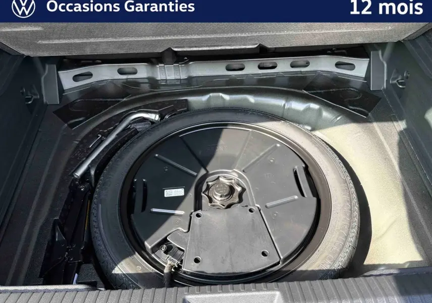 Gros plan sur la roue de secours et le cric dans le coffre ouvert d’un Volkswagen T-Roc noir.