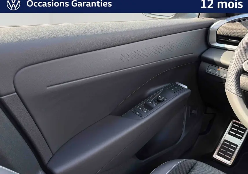 Vue intérieure côté gauche de la porte avant noire du Volkswagen T-Roc 2026 avec commandes électriques et volant partiel visible.