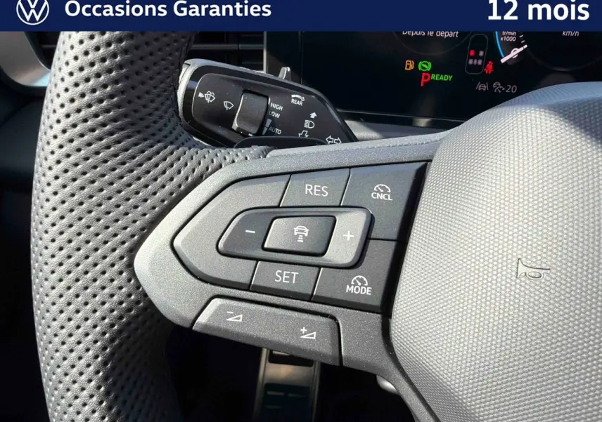 Gros plan sur le volant multifonction perforé du Volkswagen T-Roc noir, avec commandes de régulateur de vitesse et assistant de conduite.