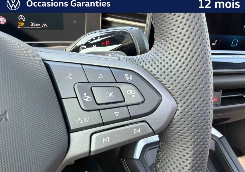 Gros plan sur le volant perforé avec commandes multifonctions du Volkswagen T-Roc noir, intérieur moderne et écran digital visible.