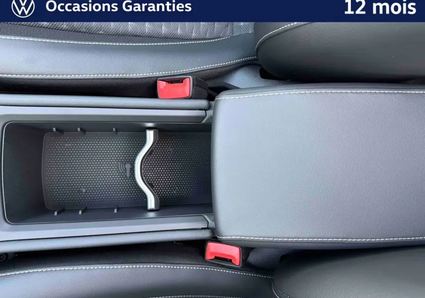 Vue plongeante sur la console centrale noire du Volkswagen T-Roc avec accoudoir et rangements ouverts.