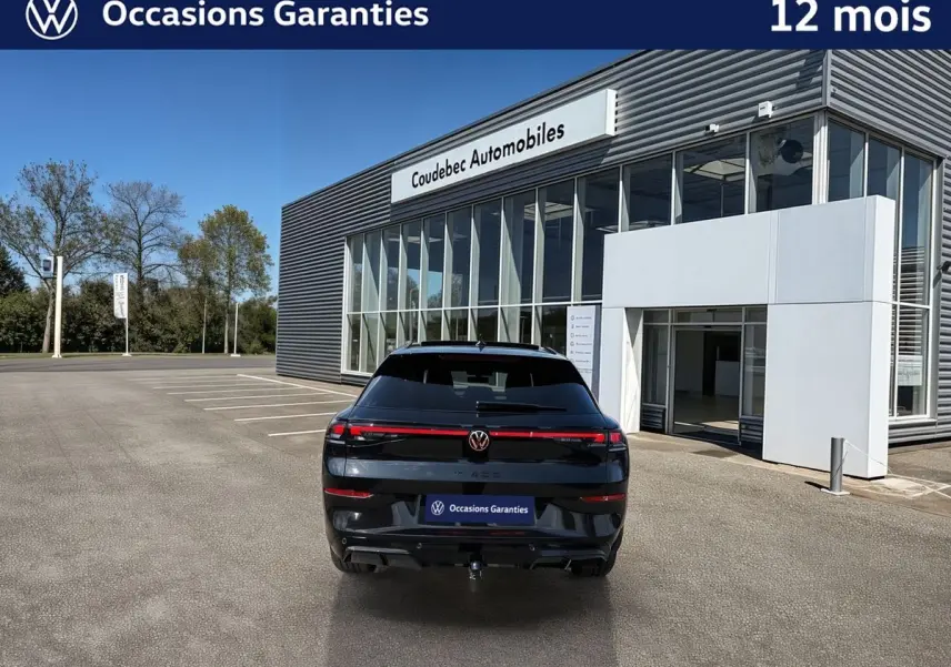 Vue arrière d'un Volkswagen T-Roc noir métallisé avec toit ouvrant panoramique et crochet d'attelage, devant un concessionnaire.