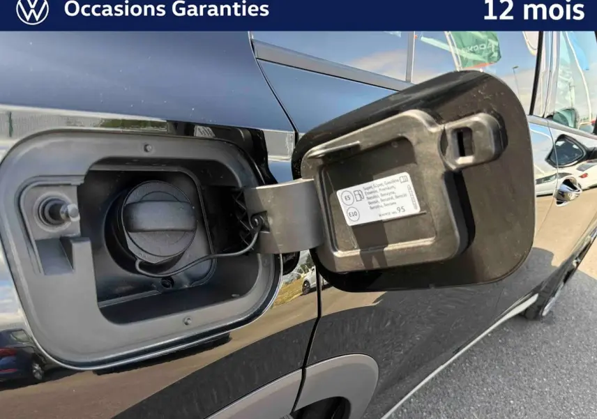 Vue rapprochée du côté gauche d’un Volkswagen T-Roc noir montrant la trappe à carburant ouverte sur un parking.