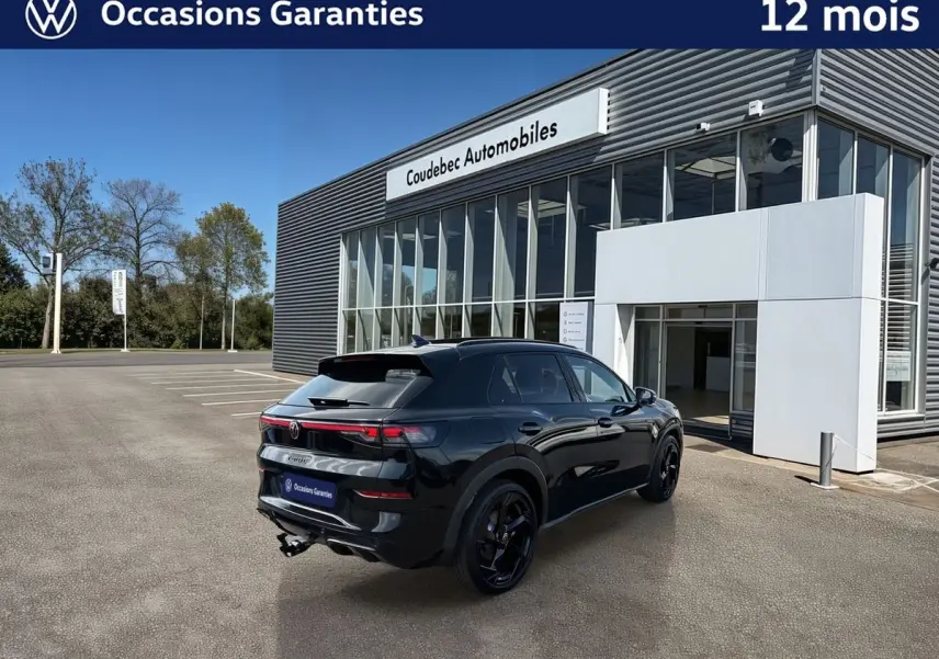 Volkswagen T-Roc noir en 3/4 arrière droit, avec jantes noires sport et crochet d'attelage escamotable visible.