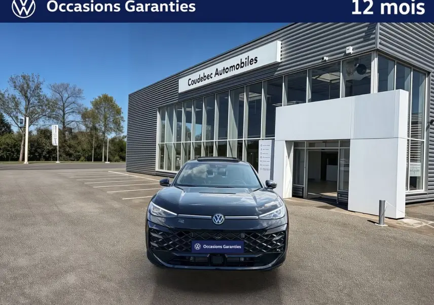 Vue de face du Volkswagen T-Roc noir métallisé avec toit ouvrant panoramique, devant un bâtiment moderne.