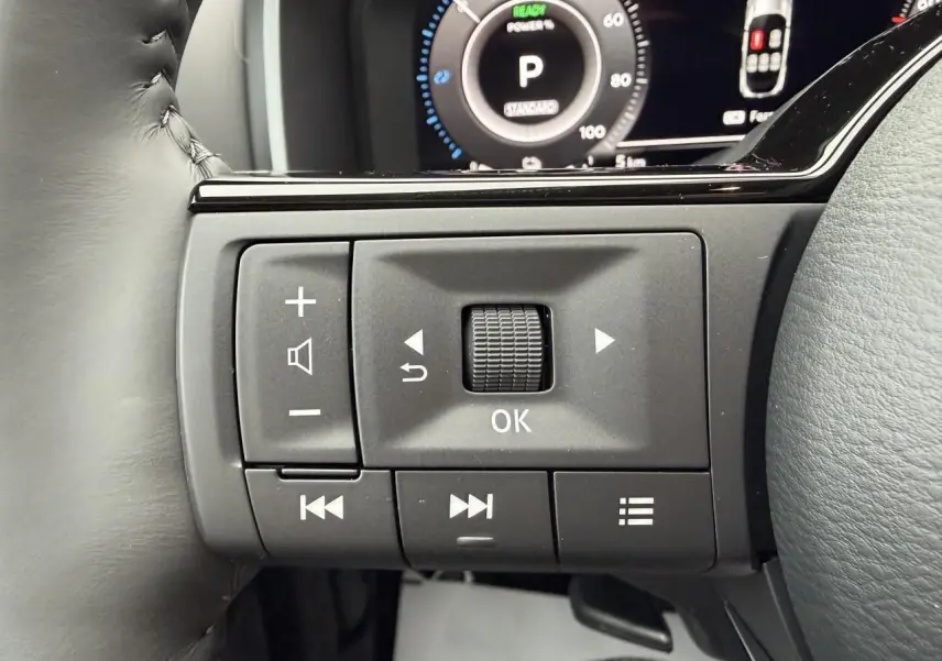 Gros plan sur les commandes au volant noir du Nissan Qashqai 2025, avec écran numérique en arrière-plan.