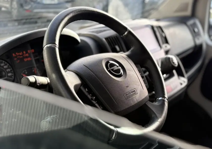 Gros plan sur le volant noir de l'Opel Movano Fourgon 2024, avec tableau de bord et commandes visibles en arrière-plan.