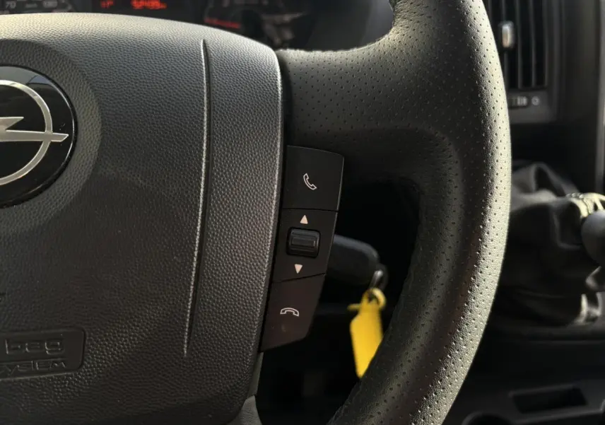Gros plan sur le volant noir perforé d’un Opel Movano 2024 avec commandes d’appel et levier de vitesses manuel visible.
