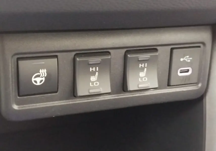 Gros plan sur les commandes de chauffage du volant et des sièges, ainsi qu’un port USB-C dans une Toyota Corolla Cross noire.